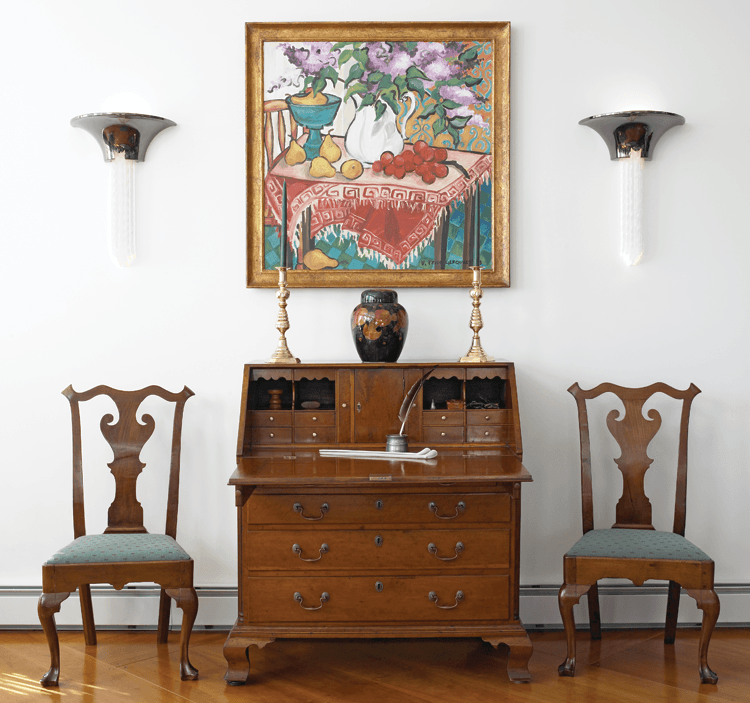 The couple found the Pennsylvania furniture through antiques dealer C. L. Prickett. The Moorcroft pomegranate ginger jar, signed Wm. Moorcraft, is flanked by nineteenth-century brass candlesticks and Art Deco sconces purchased from Rago Auctions. The wife was attracted to the 1993 painting by Blue Hill, Maine, artist Heidi Prior Gerquest, because its bold, colorful imagery complements the tones of the furniture.