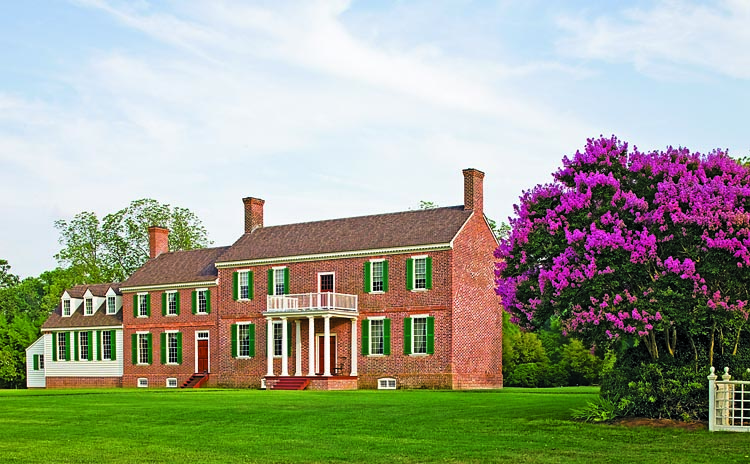 View of Mount Pleasant from the James River showing the columned porch, with its period leaded roof and wooden balustrade. The brick wing contains the family dining room, while the framed wing is a complementary modern kitchen and mudroom. One of the couple’s next projects is to recreate the historic gardens.