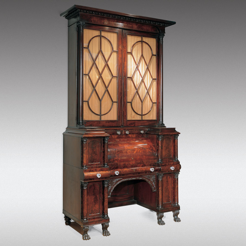 While many forms of early-nineteenth-century furniture sprung directly from Greek or Roman prototypes made of stone or bronze, many other forms created for modern use in the nineteenth century had no ancient precedent and relied, therefore, on classical architectural motifs and iconography to express the classical taste. In combination with zoomorphic and anthropomorphic elements, forms such as card tables, armoires, work tables, bureaus, and secretaries could assume an archeological flavor. In this stunning cylinder secretary bookcase the egg-and-tongue molding under the flat cornice is correctly used with the Ionic order in the upper section, and a composite capital, shown in plate 31 of Thomas Sheraton’s Cabinet Dictionary, is used in the lower case flanking all the cabinet doors. This and the carved animal paw feet establishes the classical credentials of the piece, which is otherwise drawn, in most of its details, from Sheraton’s Drawing Book and Dictionary (see illustration). It is reflective of the power of Sheraton’s work that his designs were still being incorporated into classical furniture thirty years after their publication.