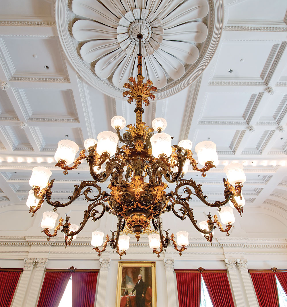 Fig. 1: Mammoth gaselier with twenty-four burners made by Cornelius & Baker for the Vermont State House in 1859. It hangs in the Representatives Chamber, and measures twenty feet high by nine feet in diameter; bronzed and gilt brass, bronzed zinc, iron. Cornelius & Baker also supplied about two dozen wall sconces for the Vermont State House at the same time, most of which survive, unlike many fixtures the firm made for the State Houses of other states. Courtesy the Vermont State Curator’s Office.