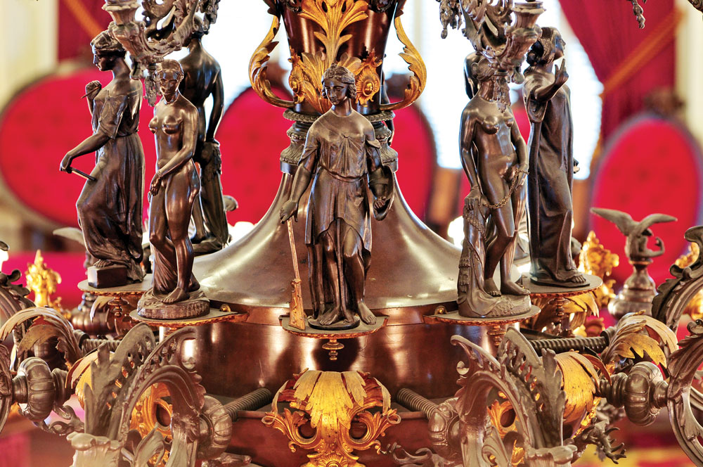 Fig. 2: Detail of the gaselier in fig. 1, showing the thirteen-inch high bronzed zinc statuettes standing between the two tiers of arms. Four of the figures are reductions of Hiram Powers’ celebrated marble statue of the Greek Slave. They alternate with allegorical figures representing Commerce, Science, Prudence and Eloquence. Courtesy of the Vermont State Curator’s Office.