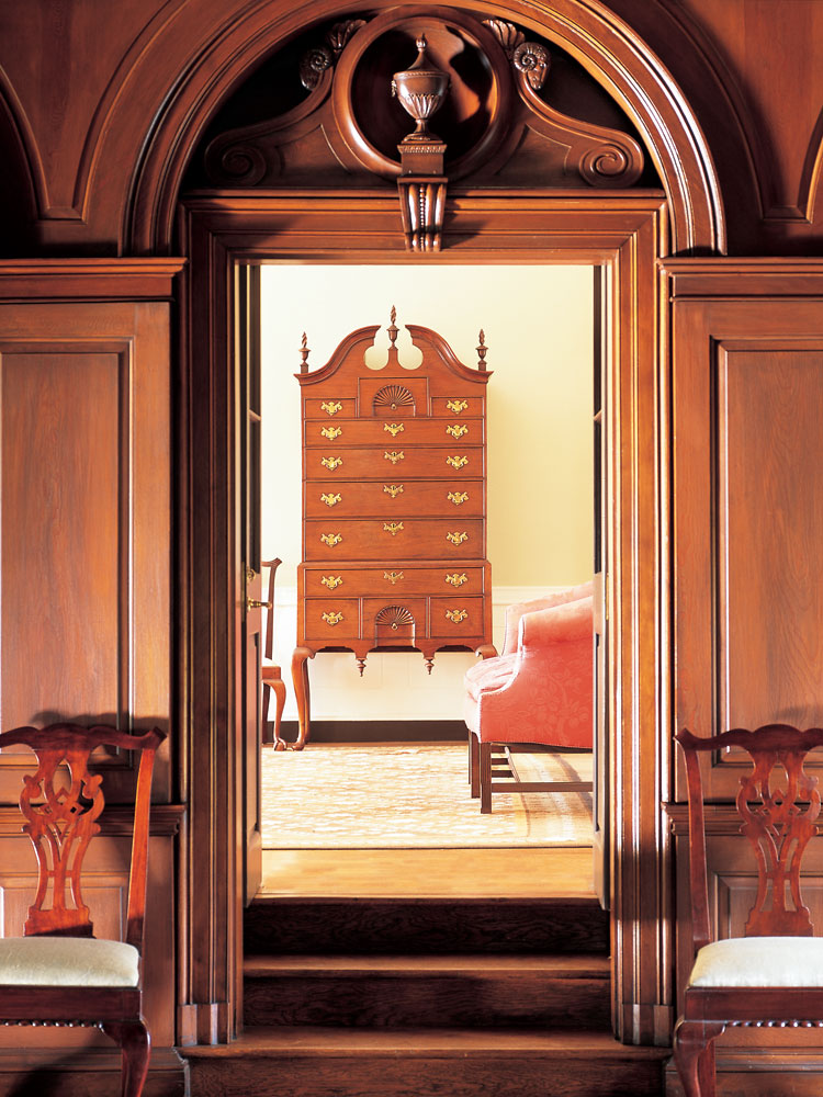 Architect William Lawrence Bottomley’s (1883–1951) mastery of design skills can be seen in his promiscuous combination of elements in the paneled library doorway. The scrolled-top walnut high chest, from the third quarter of the eighteenth century, has impeccable proportions which was a factor in the couple’s purchase — as was the signature of the maker, Thomas Howard of Boston. Two New York side chairs grace the entry into the living room from the library.