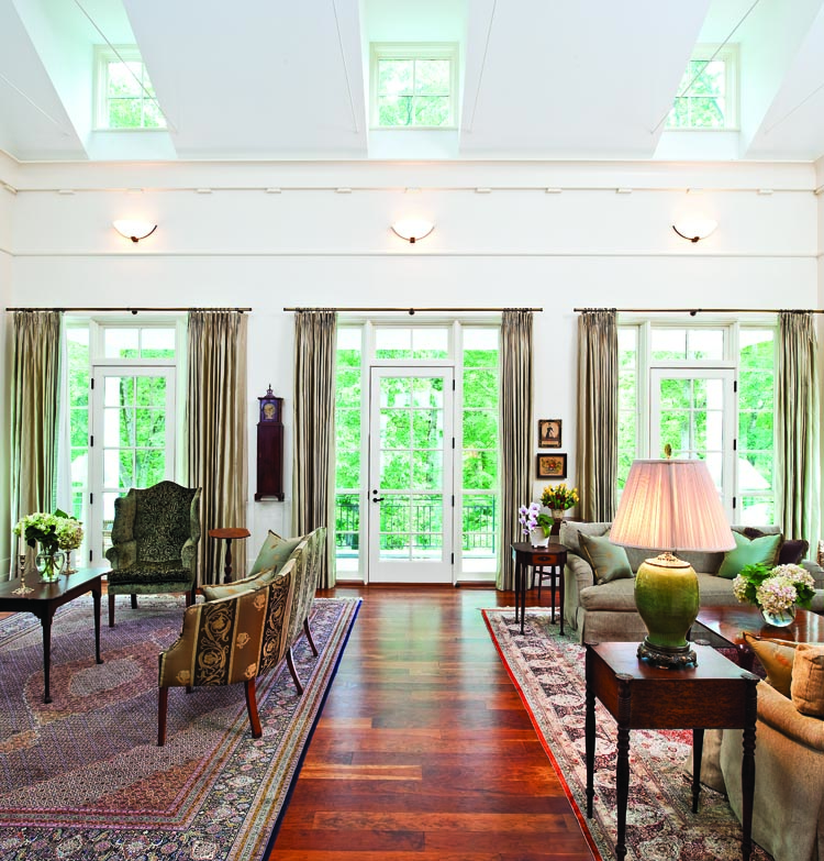 The ceiling height and abundant light make the great room a natural display area for many of the couple’s interests. The two stands beside the matching sofas reflect the owners’ interest in both form and surface quality. One, with a dramatically shaped top and unusual inlay is made of cherry; the other with carved rosettes applied to the corners of the top is made completely of bird’s-eye maple. Each stand retains its original surface. On the far wall to the right of the double doors to the patio, is the colorful J. H. Davis watercolor of seventeen-year-old Dorinda York painted in 1837, and pictured in Three American Watercolor Painters (1974), by Gail and Norbert Savage. A small theorem of fruit depicts a Canton ware bowl, circa 1830. Beneath is an octagonal-topped sewing stand with an inlaid and molded-edge lift top, inlaid facade, and with line-inlaid splayed legs and cross-stretchers. This rare stand is made of mahogany, retains its original surface, and was probably made in Newburyport, Mass. or Portsmouth, N.H., circa 1800. To the left of the door is one of three known “grandmother” clocks attributed to the Mulliken family of clockmakers. The others are pictured in Nutting’s Furniture Treasury (1928) and Brooks Palmer’s The American Clock (1928).