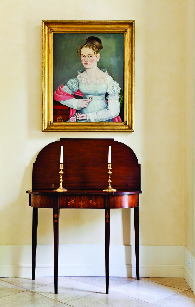 Some of the pieces of most importance to the collectors are displayed in the foyer. A Federal card table, probably made in or near Providence, R.I, circa 1800, is one of the finest examples of the form. Above it is a portrait of Kate Elting, painted in New Paltz, New York, probably in 1824. The sitter’s white dress shows the artist’s ability to adroitly picture transparent fabric. Kate leans on the edge of a table that is still in the Elting family house in New Paltz, now owned by the Huguenot Society, and in which portraits of other members of her family still hang. The original gilded leaf and berry frame is labeled by its maker, “Bernard/Carver, Gilder, and Looking—Glass Manufactgurer/1-2 Warren Street (New York City);” the firm was at this location only in 1824.