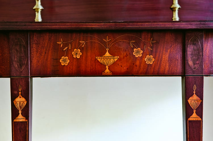 The quality of the inlay work on this Rhode Island card table in the foyer is matched by the original finish and condition. The covered urns on the legs, rather than on the plinths, which are composed of grained mahogany, are an unusual and attractive treatment.